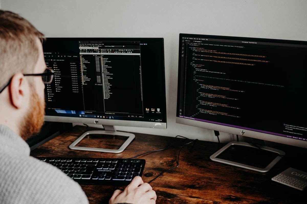 Two monitors showing an application front end beside its source code